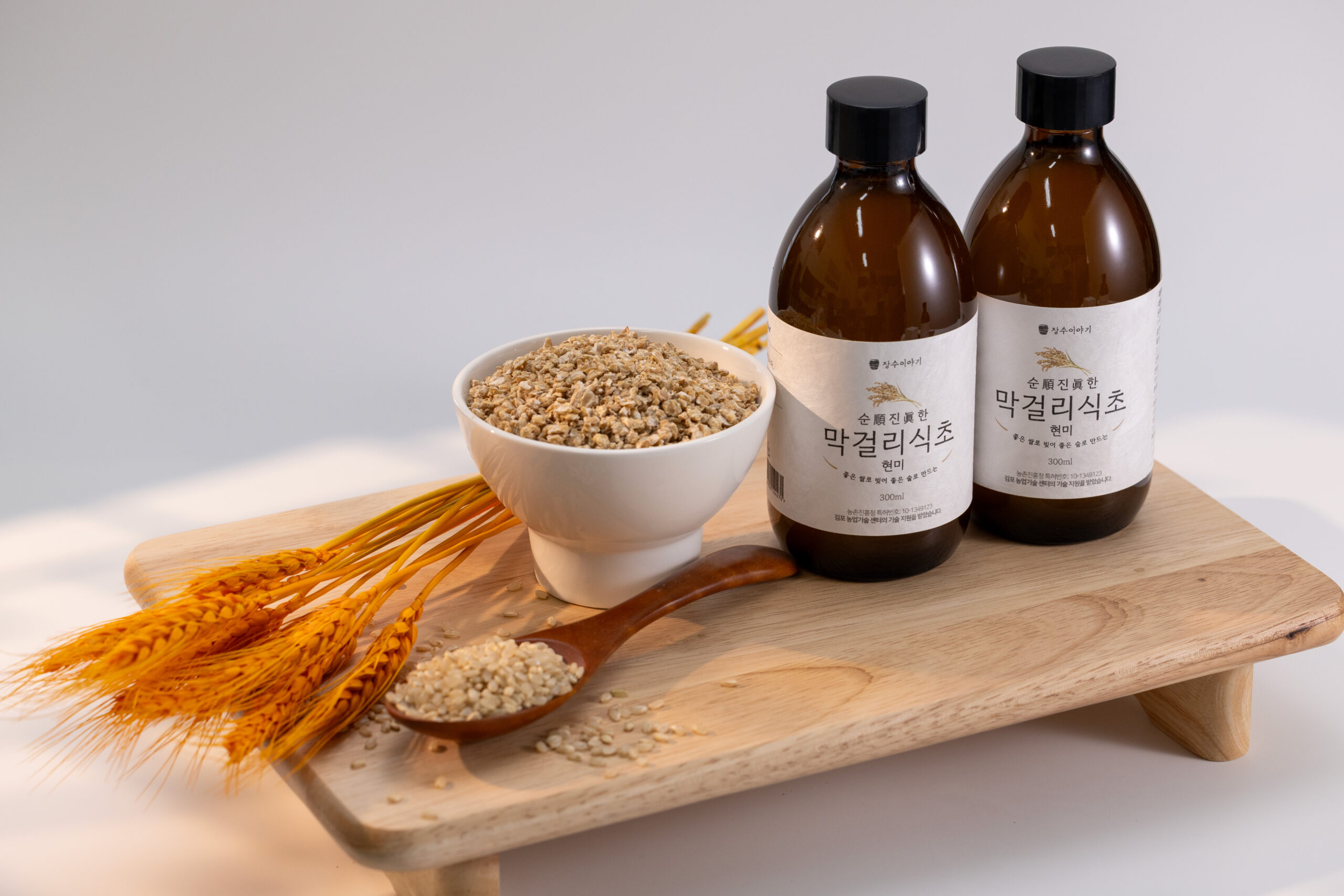 Makgeolli vinegar bottles on a wooden tray with brown rice and wheat